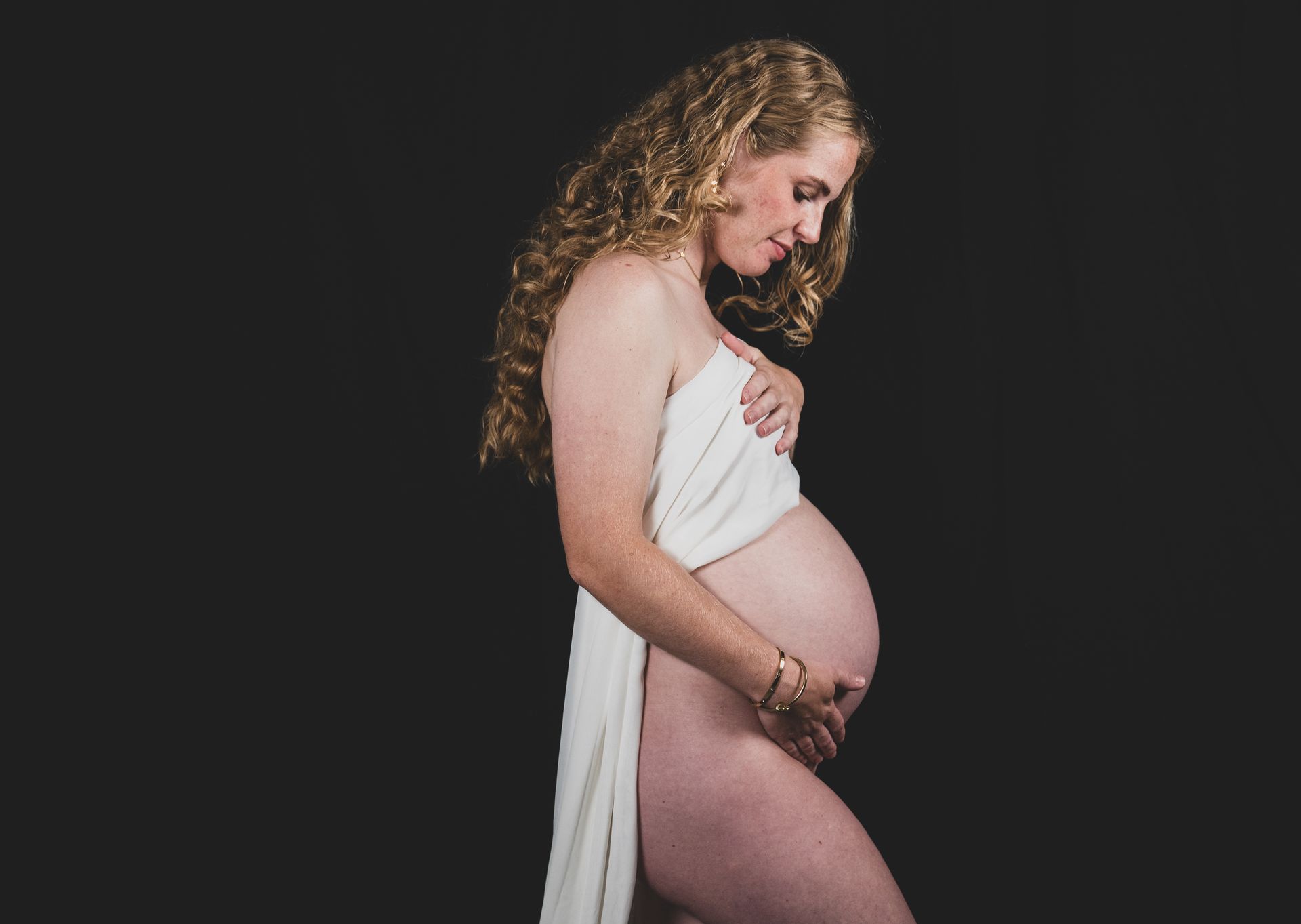 Koppel zwangerschapsfoto – man kust zwangere vrouw op wang, emotionele zwangerschapsshoot op locatie